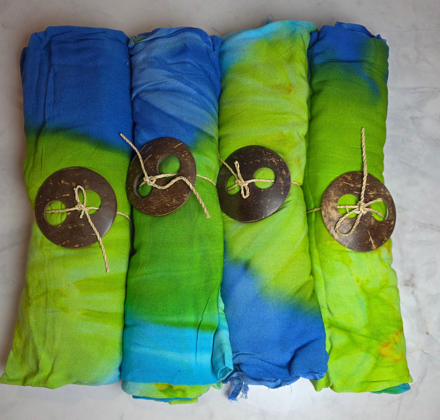 Stack of folded tie-dye sarongs with circular brown labels on a light gray surface.